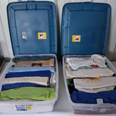 Two large plastic storage totes filled with organized, neatly folded graphic T-shirts.