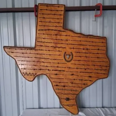 Large wooden Texas-shaped barbed wire display plaque, featuring various labeled antique wire samples, a central horseshoe accent, and...