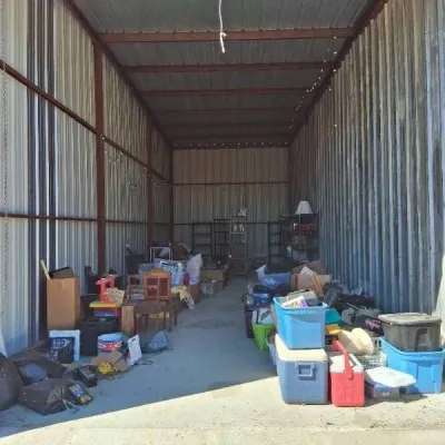 Large outdoor storage unit or shed filled with assorted household goods, plastic storage totes, coolers, and small furniture.