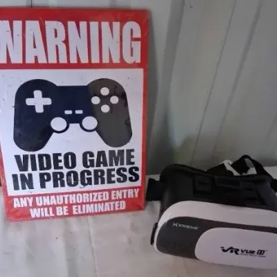 Novelty metal sign reading "Warning: Video Game In Progress" displayed alongside a VR Vue II virtual reality headset.