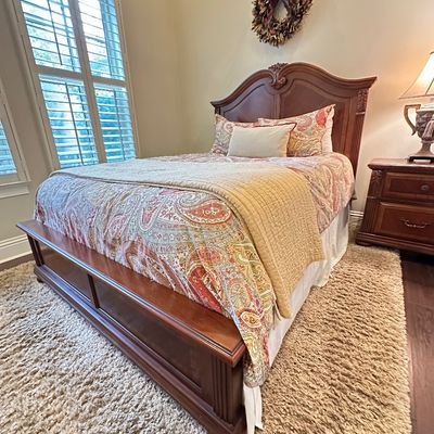Sale Photo Thumbnail #118: Traditional carved wood bed frame set with matching nightstand, dressed in a paisley comforter and decorative pillows.