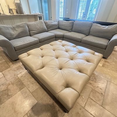 Sale Photo Thumbnail #10: Large grey fabric sectional sofa with rolled arms paired with a square cream leather button-tufted oversized ottoman.