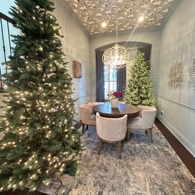 Sale Photo Thumbnail #84: Contemporary dining room set featuring a round dark wood table and four beige upholstered barrel chairs, framed by pre-lit artificial Christmas trees.