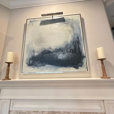 Sale Photo Thumbnail #7: Large contemporary abstract canvas painting framed in silver-tone metal, flanked by a pair of wooden candlestick holders on a fireplace mantle.