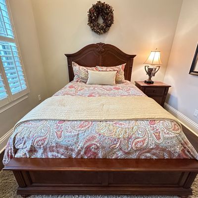 Sale Photo Thumbnail #117: Traditional dark wood bed frame with carved arched headboard, dressed in a paisley comforter set with matching nightstand and table lamp.