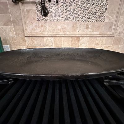 Sale Photo Thumbnail #40: Large oval cast iron or dark metal serving platter resting on a stovetop, featuring a textured interior finish.