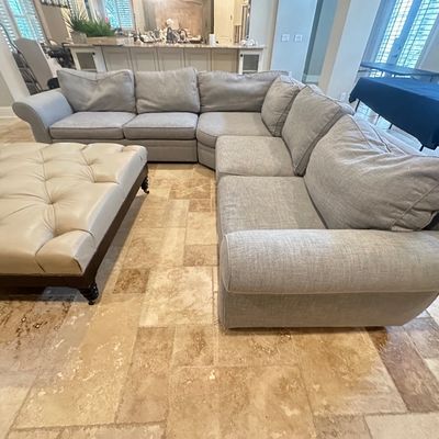 Sale Photo Thumbnail #11: Large light gray sectional sofa paired with a cream leather tufted ottoman featuring nailhead trim.