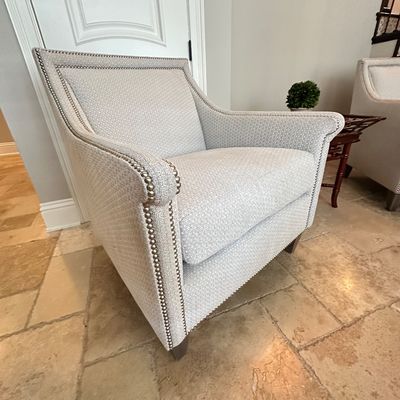 Sale Photo Thumbnail #110: Contemporary armchair with light gray patterned upholstery and silver nailhead trim. Features tapered wooden legs and a sloped arm design in good condition.