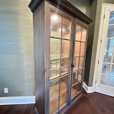 Sale Photo Thumbnail #113: Traditional wooden display cabinet with a weathered grey-brown finish, glass-paned doors, interior lighting, and adjustable glass shelves.