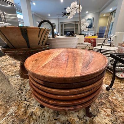 Sale Photo Thumbnail #37: Stack of round wooden charger plates or serving trays set on a kitchen counter, flanked by ceramic bowls and glassware.