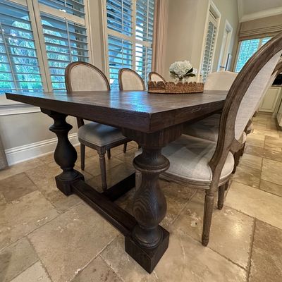 Sale Photo Thumbnail #52: Rustic wood trestle dining table with dark finish and large baluster legs, surrounded by upholstered oval-back dining chairs in French country style.