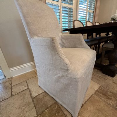 Sale Photo Thumbnail #50: High-back fully slipcovered dining armchair in light beige fabric, placed next to a dark wood dining table.