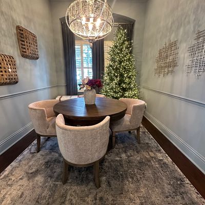 Sale Photo Thumbnail #85: Round dark wood dining table set with four upholstered barrel chairs, complemented by an ornate mercury glass chandelier and a lit Christmas tree in the background.