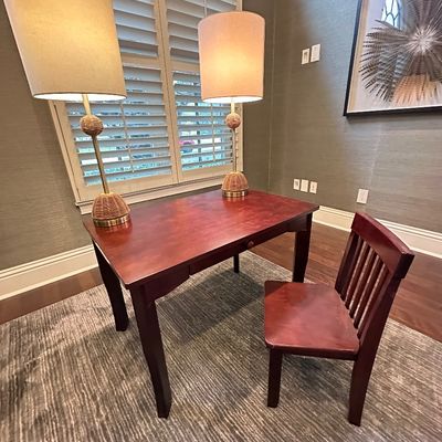 Sale Photo Thumbnail #57: Reddish-brown wooden desk set with a single slat-back chair, paired with a matching set of two tall table lamps featuring woven rattan accents and beige drum shades.