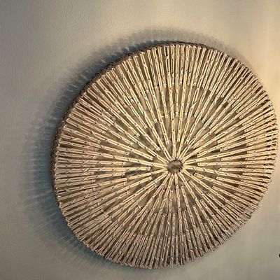 Sale Photo Thumbnail #29: Large circular woven wicker or seagrass wall hanging with a sunburst pattern, mounted on a neutral wall.