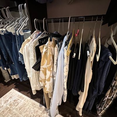 Sale Photo Thumbnail #58: A rack of women's clothing featuring casual tops, blouses, and trousers, alongside blue denim jeans hanging in a organized closet space.
