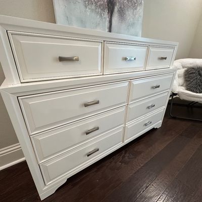 Sale Photo Thumbnail #82: Modern white wooden dresser featuring nine drawers with brushed metal pulls and beveled panel fronts.