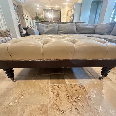 Sale Photo Thumbnail #13: Large cream leather tufted ottoman featuring nailhead trim details and dark turned wooden legs on casters.