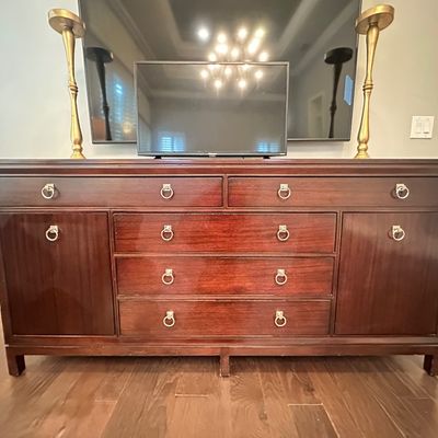 Sale Photo Thumbnail #99: Traditional mahogany buffet server with brass ring pulls, flanking cabinets, and multiple drawers, topped with a small flat-screen television and brass floor lamps.