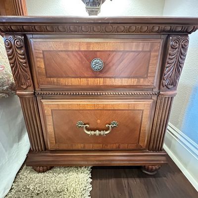 Sale Photo Thumbnail #119: Traditional style wooden nightstand featuring carved decorative columns, inlaid wood drawer fronts, and metal hardware.