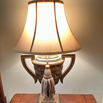 Sale Photo Thumbnail #116: Traditional trophy-style table lamp featuring a textured ceramic urn base, two side handles, hanging tassel detail, and a bell shade.