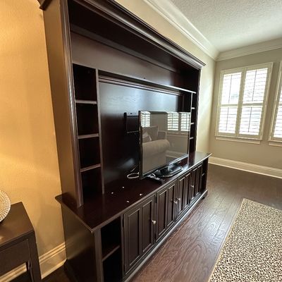 Sale Photo Thumbnail #31: Large dark espresso-finished wooden entertainment center with upper bridge hutch, side shelving, and lower cabinet storage, featuring a flat-screen television.