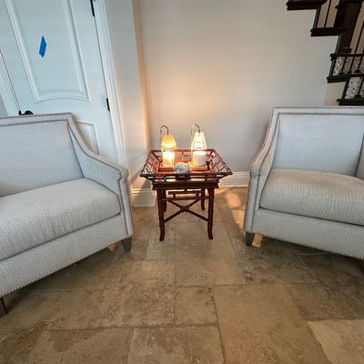 Sale Photo Thumbnail #33: Pair of contemporary light gray upholstered accent armchairs with nailhead trim, flanking a faux-bamboo wooden side table.