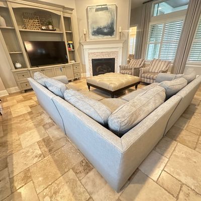 Sale Photo Thumbnail #89: Large light grey fabric sectional sofa paired with a tufted leather ottoman and matching striped armchairs in a spacious living room.