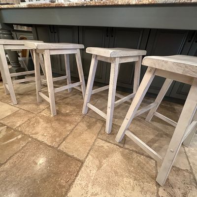 Sale Photo Thumbnail #35: Set of four distressed white wooden bar stools featuring saddle seats and A-frame legs.