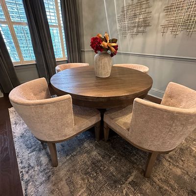 Sale Photo Thumbnail #104: Contemporary round dark wood dining table set with four upholstered curved-back barrel chairs, styled with a ribbed ceramic vase centerpiece.