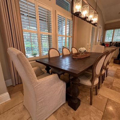 Sale Photo Thumbnail #51: Rustic dark wood dining table set with upholstered oval-back chairs and slipcovered captain's chairs, suspended under a modern industrial metal chandelier.