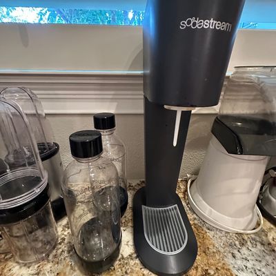 Sale Photo Thumbnail #45: Black SodaStream sparkling water maker shown with two reusable carbonating bottles and other small kitchen appliances.