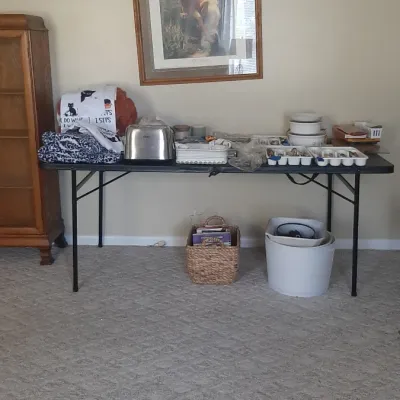 Folding table displaying various household items, including a toaster, kitchenware, linens, and framed wall art above.