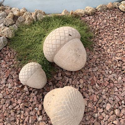 Sale Photo Thumbnail #137: Set of three concrete or stone acorn-shaped garden sculptures, featuring crosshatch-textured caps and a weathered finish.
