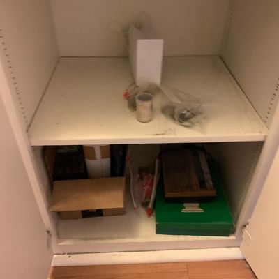 Sale Photo Thumbnail #96: White built-in cabinet shelves containing miscellaneous household supplies, boxed items, and a vintage paper shredder or office accessory.
