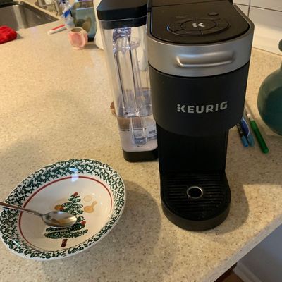 Sale Photo Thumbnail #78: Black Keurig single-serve coffee maker with removable side water reservoir, sitting on a kitchen countertop next to a Christmas-themed bowl.