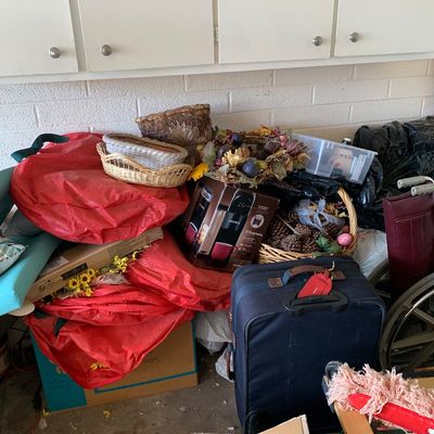 Sale Photo Thumbnail #48: Assorted household items including a Keurig K-Supreme coffee maker in box, navy blue rolling suitcase, decorative baskets, floral wreaths, and storage bags beneath white wall cabinets.