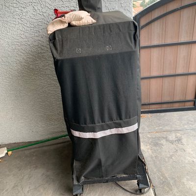 Sale Photo Thumbnail #38: Large outdoor vertical smoker or grill on caster wheels, protected by a fitted black fabric cover.