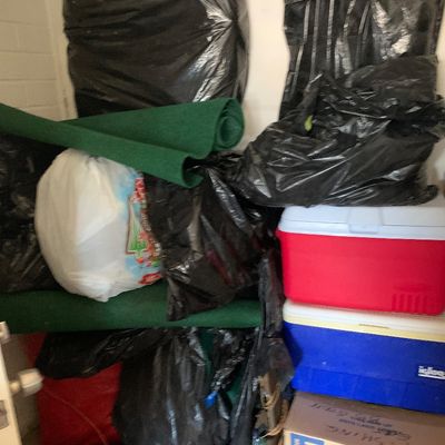 Sale Photo Thumbnail #57: Assorted stored items, including plastic bags, rolled green felt matting, Igloo coolers, and a Lowe's moving box stacked in a closet or storage area.