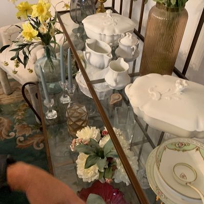 Sale Photo Thumbnail #131: Two-tier glass and metal server table display featuring white ceramic serving pieces, floral arrangements in glass vases, clear glass candle holders, and vintage china.