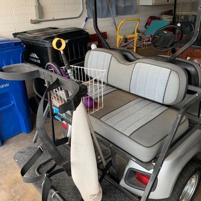 Sale Photo Thumbnail #51: EZGO golf cart featuring gray vinyl patterned seats, a rear bag attachment bracket, and an attached storage basket, parked in a garage.