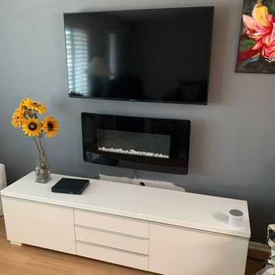 Sale Photo Thumbnail #5: Modern wall-mounted flat-screen TV above an electric fireplace insert and a long white low-profile media console.