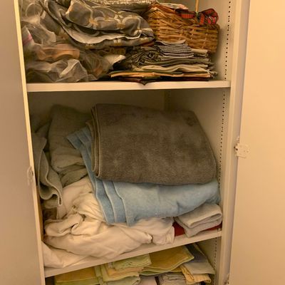 Sale Photo Thumbnail #95: White storage cabinet filled with assorted linens, towels, fabric remnants, and a woven basket.