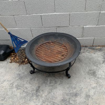Sale Photo Thumbnail #39: Round metal outdoor fire pit on scroll legs with a rusted interior grate, set against a cinder block wall.