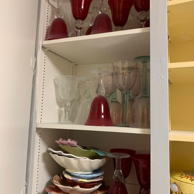 Sale Photo Thumbnail #33: A cupboard filled with glassware, featuring ruby red wine glasses with clear stems and a stack of colorful ceramic decorative dishes.