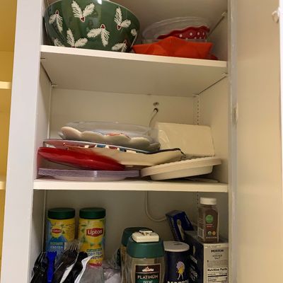 Sale Photo Thumbnail #31: Open white kitchen cabinet filled with various items including holiday serving bowls, stacked plates, Morton salt, Lipton iced tea mix, and plastic utensils.