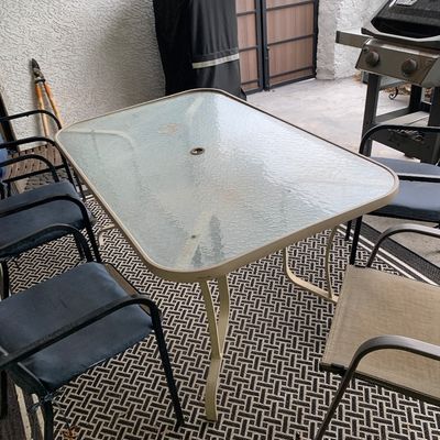 Sale Photo Thumbnail #35: Outdoor glass-top patio dining table with an umbrella hole, accompanied by several metal patio armchairs.