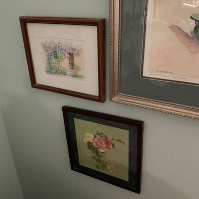 Sale Photo Thumbnail #87: Collection of three framed wall art pieces, including a watercolor of a floral doorway, a floral print in a dark frame, and a large coastal artwork in a silver-toned frame.