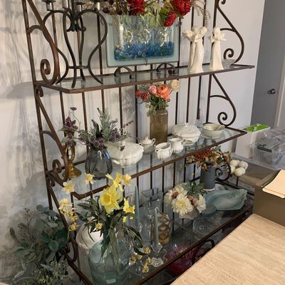 Sale Photo Thumbnail #11: Wrought iron baker's rack with glass shelves, styled with home decor, faux floral arrangements, and porcelain serving pieces.