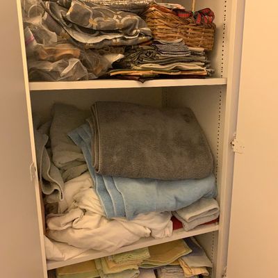 Sale Photo Thumbnail #94: White storage cabinet filled with assorted household linens, folded towels, bed sheets, fabric remnants, and a woven basket.